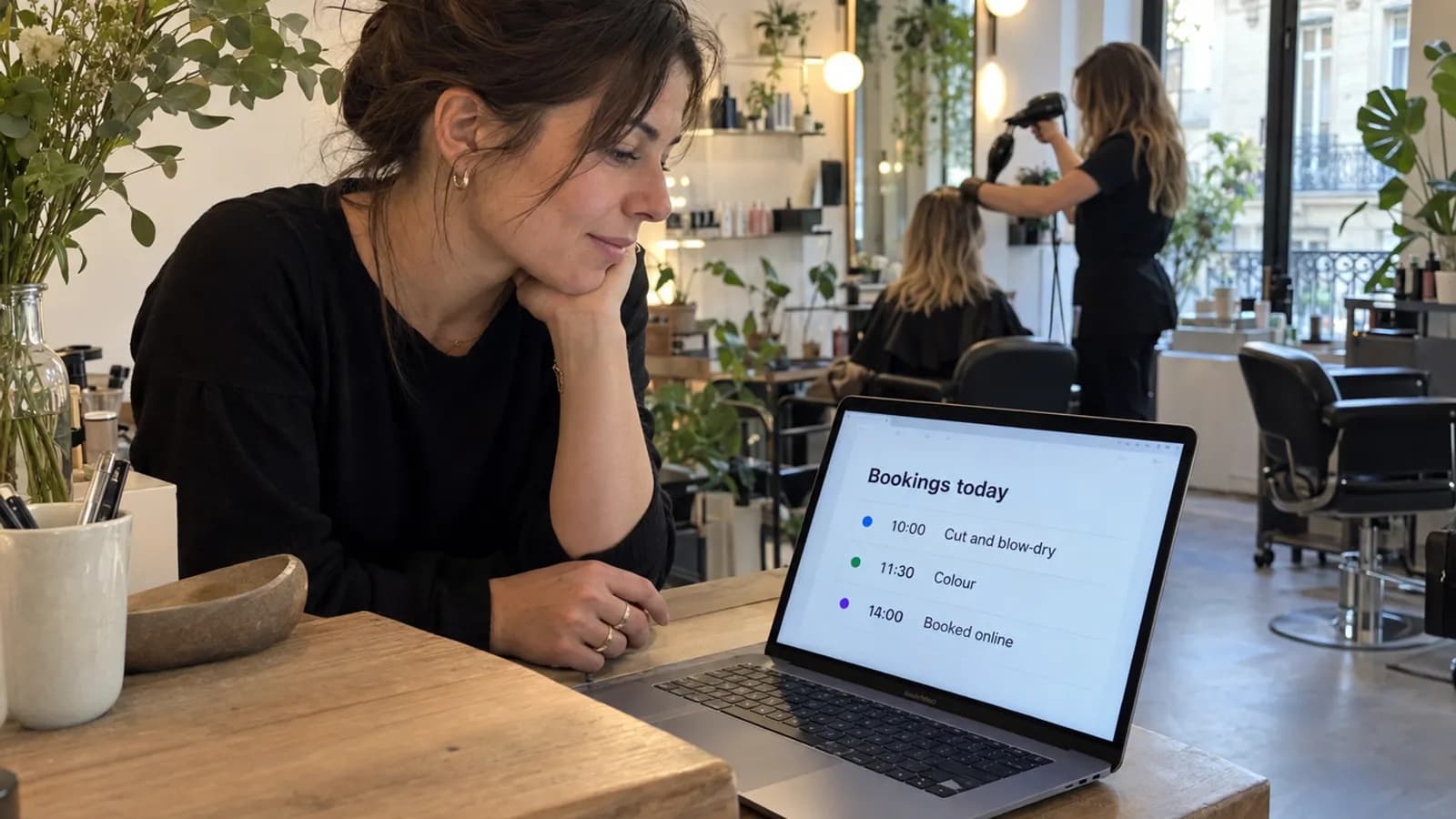 Salon owner checking the day's online bookings on a laptop at reception